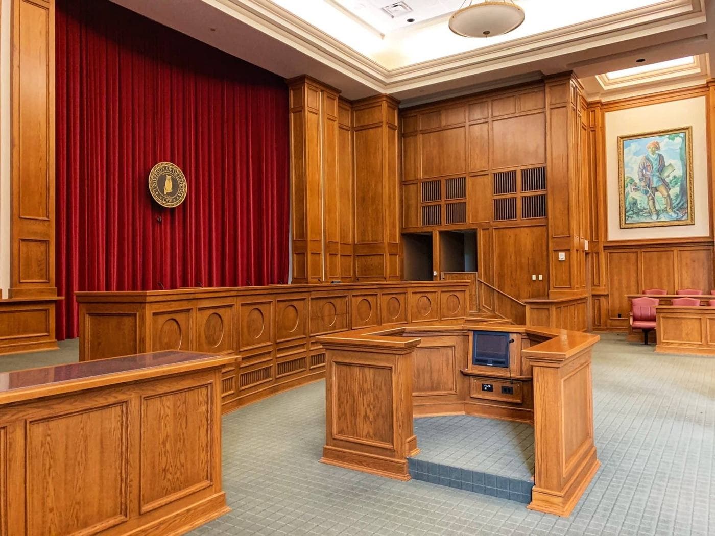 Empty wood-paneled courtroom with a red curtain and witness stand