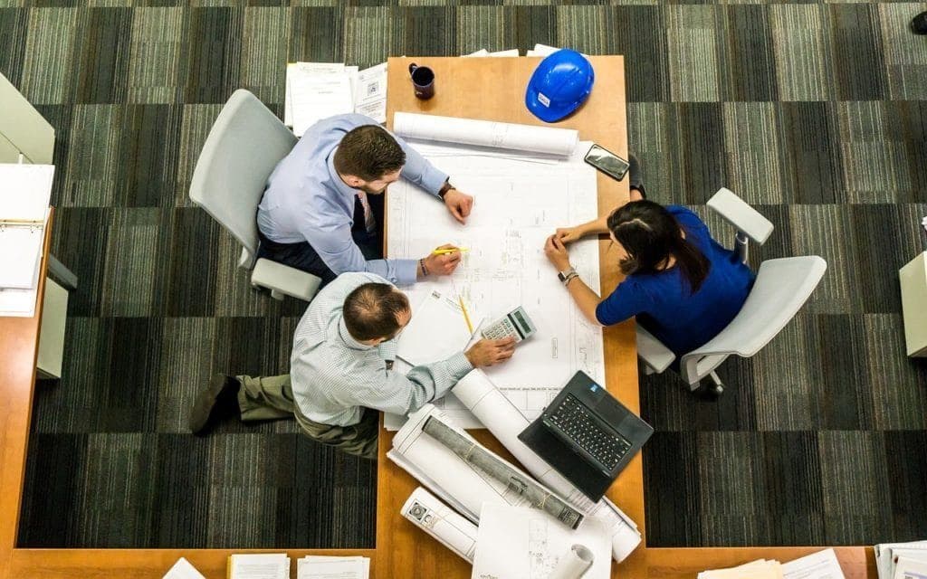 Construction team reviewing building plans around a table, seen from above